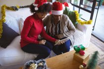 Счастливая африканская старшеклассница и взрослая дочь в шляпах Санты делают рождественский видеозвонок. Рождество, праздник и коммуникационные технологии. — стоковое фото