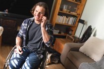 Caucasiano deficiente homem sentado em cadeira de rodas falando no smartphone em casa. conceito de deficiência e deficiência — Fotografia de Stock