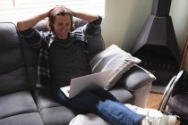 Homem deficiente caucasiano sorrindo usando laptop sentado no sofá em casa. conceito de deficiência e deficiência — Fotografia de Stock