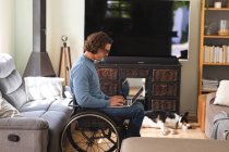 Кавказький інвалід у окулярах сидить на інвалідному візку, використовуючи ноутбук удома. інвалідність і гандикап — стокове фото