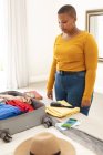African american plus size woman packing suitcase for travel. travel preparation during covid 19 pandemic. — Stock Photo