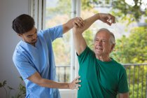 Zweirassiger männlicher Physiotherapeut, der Arme eines älteren männlichen Patienten in der Klinik behandelt. Senior Health und medizinische physiotherapeutische Behandlung. — Stockfoto