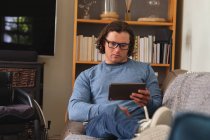 Белый инвалид в очках с цифровой планшеткой сидит дома на диване. Концепция инвалидности и инвалидности — стоковое фото