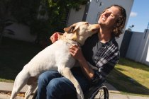 Кавказький інвалід сидить на інвалідному візку граючись зі своїм собакою на дорозі. інвалідність і гандикап — стокове фото