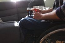 Mittelteil eines behinderten Mannes, der im Rollstuhl sitzt und zu Hause eine Kaffeetasse hält. Behinderten- und Behindertenkonzept — Stockfoto