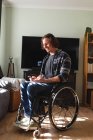 Homem deficiente caucasiano sentado em cadeira de rodas sorrindo enquanto usa smartphone em casa. conceito de deficiência e deficiência — Fotografia de Stock