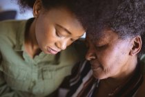 Mujer mayor afroamericana con hija adulta abrazando con los ojos cerrados. tiempo en familia en casa juntos. - foto de stock