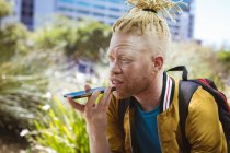 Heureux albinos homme afro-américain avec dreadlocks dans le parc parler sur smartphone. nomade numérique en déplacement, en déplacement dans la ville. — Photo de stock