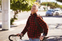 Ritratto di sorridente uomo afroamericano albino con dreadlocks in strada con bici. in movimento, in giro per la città. — Foto stock