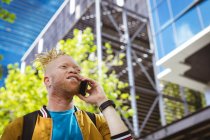 Glücklicher Albino-Afrikaner mit Dreadlocks im Park, der mit dem Smartphone spricht. digitaler Nomade unterwegs, unterwegs in der Stadt. — Stockfoto