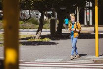 Hombre afroamericano albino con mascarilla facial y rastas caminando y usando smartphone. sobre la marcha, fuera y alrededor de la ciudad durante la pandemia covid 19. - foto de stock