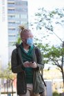 Альбіно- африканського американця з маскою обличчя і дредами, що ходять і користуються смартфоном. в дорозі, і в околицях міста під час зажерливості 19. — стокове фото