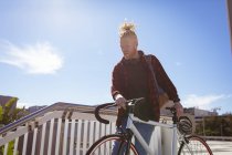 Thoughtful albino african american man with dreadlocks going down stairs with bike. on the go, out and about in the city. — Stock Photo