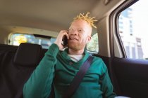 Heureux albinos homme afro-américain avec dreadlocks assis dans la voiture parler sur smartphone. nomade numérique en déplacement, en déplacement dans la ville. — Photo de stock