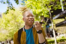 Счастливый афроамериканец-альбинос с дредами в парке разговаривает по смартфону. цифровая реклама на ходу, на улице и по городу. — стоковое фото