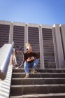 Pensativo albino hombre afroamericano con rastas usando auriculares usando teléfono inteligente. nómada digital sobre la marcha, fuera y alrededor de la ciudad. - foto de stock