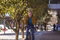 Réfléchi albinos homme afro-américain avec dreadlocks vélo d'équitation. on the go, out and about dans la ville. — Photo de stock