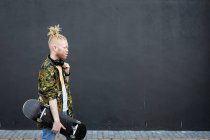 Felice uomo afroamericano albino con dreadlocks che cammina tenendo lo skateboard. in movimento, in giro per la città. — Foto stock