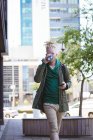 Homme américain albinos réfléchi avec dreadlocks boire du café à l'aide d'un smartphone. nomade numérique en déplacement, en déplacement dans la ville. — Photo de stock