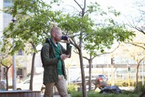 Pensativo albino homem americano africano com dreadlocks beber café usando smartphone. nômade digital em movimento, para fora e sobre na cidade. — Fotografia de Stock