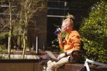 Thoughtful albino african american man with dreadlocks sitting in park drinking coffee using laptop. digital nomad on the go, out and about in the city. — Stock Photo
