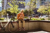 Albino hombre afroamericano con rastas sentado en el parque con la bicicleta comer sándwich. sobre la marcha, fuera y alrededor de la ciudad. - foto de stock