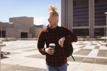 Pensativo albino hombre afroamericano con rastas usando smartwatch. nómada digital sobre la marcha, fuera y alrededor de la ciudad. - foto de stock