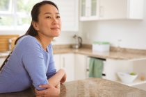 Porträt einer glücklichen asiatischen Frau, die am Tisch in der Küche sitzt. Lebensstil, Freizeit und Zeit zu Hause verbringen. — Stockfoto