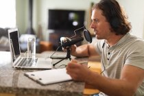 Белый человек записывает подкаст с помощью микрофона, сидя дома. концепция блогов, подкастов и радиовещательных технологий — стоковое фото