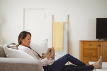 Konzentrierte Asiatin, die zu Hause auf dem Sofa mit Tablet sitzt. Lifestyle und Entspannung zu Hause mit Technologie. — Stockfoto