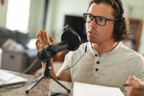 Homme caucasien enregistrement podcast en utilisant un microphone assis à la maison. blogging, podcast et concept de technologie de radiodiffusion — Photo de stock