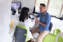 Усміхаючись жінка-стоматолог вивчає зуби пацієнта чоловічої статі в сучасній стоматологічній клініці. охорона здоров'я та стоматологічний бізнес . — стокове фото