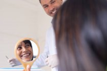 Lächelnder kaukasischer Zahnarzt mit Patientin im Spiegel einer modernen Zahnklinik. Gesundheits- und Zahnarztgeschäft. — Stockfoto