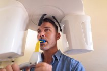 Paciente masculino caucásico que examina dientes y se somete a rayos X en una clínica dental moderna. negocio de salud y odontología. - foto de stock