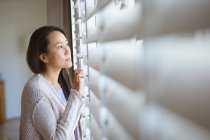 Profil einer nachdenklichen asiatischen Frau, die am Fenster steht und nach draußen schaut. Lebensstil, Freizeit und Zeit zu Hause verbringen. — Stockfoto