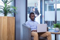Uomo d'affari afroamericano che utilizza laptop con colleghi in background in un ufficio moderno. lavoro d'affari e d'ufficio. — Foto stock