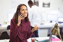 Donna d'affari birazziale felice che parla su smartphone con colleghi in background in ufficio moderno. lavoro d'affari e d'ufficio. — Foto stock