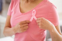 Midsection of asian woman in pink tshirt showing breast cancer awareness pink ribbon at home. health, prevention and breast cancer awareness. — Stock Photo