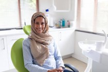 Portrait of smiling biracial female patient sitting at modern dental clinic. healthcare and dentistry business. — Stock Photo