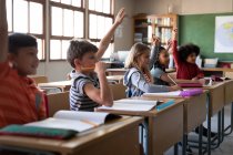 Eine Gruppe multiethnischer Kinder sitzt auf ihrem Schreibtisch im Klassenzimmer der Schule. Grundschulbildung soziale Distanzierung der Gesundheitssicherheit während der Covid19 Coronavirus-Pandemie. — Stockfoto