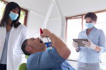 Двосторонній жіночий стоматолог з медсестрою вивчає зуби пацієнта чоловічої статі в сучасній стоматологічній клініці. охорона здоров'я та стоматологічний бізнес . — стокове фото