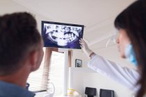 В современной стоматологической клинике бразильская женщина-стоматолог в маске для лица осматривает зубы пациента мужского пола. здравоохранение и стоматология. — стоковое фото