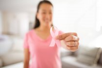 Mulher asiática em camiseta rosa mostrando a consciência do câncer de mama fita rosa em casa. saúde, prevenção e sensibilização para o cancro da mama. — Fotografia de Stock