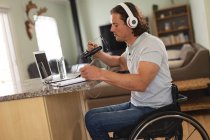 Hombre caucásico discapacitado grabando podcast usando micrófono sentado en una silla de ruedas en casa. concepto de blogging, podcast y tecnología de radiodifusión - foto de stock