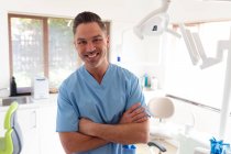 Porträt eines lächelnden kaukasischen Zahnarztes, der in die Kamera einer modernen Zahnklinik blickt. Gesundheits- und Zahnarztgeschäft. — Stockfoto