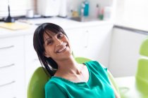 Portrait d'une patiente biraciale souriante regardant une caméra dans une clinique dentaire moderne. soins de santé et de la dentisterie. — Photo de stock