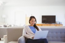 Feliz mulher asiática sentada no sofá com laptop em casa. estilo de vida e relaxar em casa com a tecnologia. — Fotografia de Stock