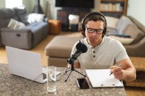Homem caucasiano gravando podcast usando microfone sentado em casa. conceito de tecnologia de blogging, podcast e radiodifusão — Fotografia de Stock
