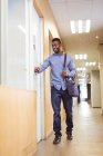 Empresário afro-americano sorridente andando e abrindo a porta no corredor no escritório moderno. empresa e escritório local de trabalho. — Fotografia de Stock