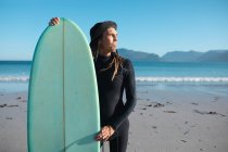 Männliche Surfer stehen mit blauem Surfbrett am sonnigen Tag am Strand und schauen weg. Hobbys und Wassersport. — Stockfoto